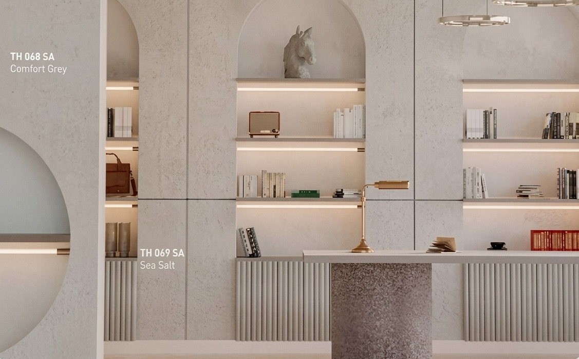 Inspirasi desain interior ruang kerja minimalis yang elegan. Menampilkan rak dinding dengan pencahayaan LED tersembunyi, menggunakan paduan HPL Taco kodeTH 068 SA Comfort Grey dan TH 069 SA Sea Salt. Terdapat meja dengan aksen teraso, dekorasi buku, patung kuda, dan lampu meja brass